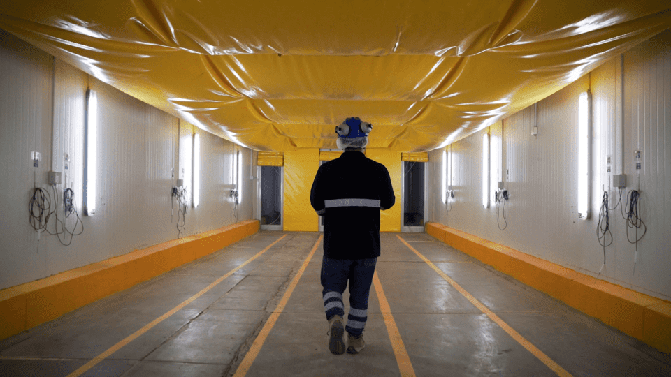 Un trabajador con casco, chaleco reflectante y botas de trabajo camina por el pasillo de un túnel californiano.